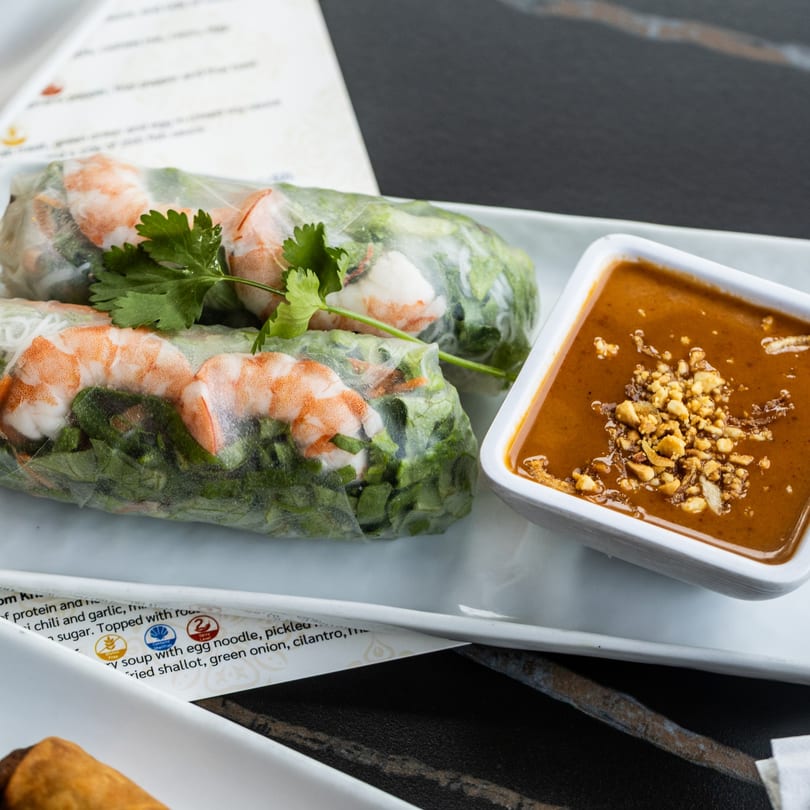 Two fresh spring rolls with shrimp and greens, served with peanut dipping sauce and a menu.
